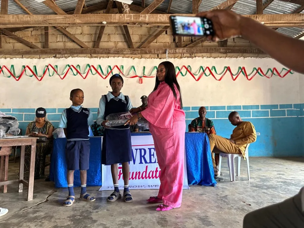 woman giving items to 2 students